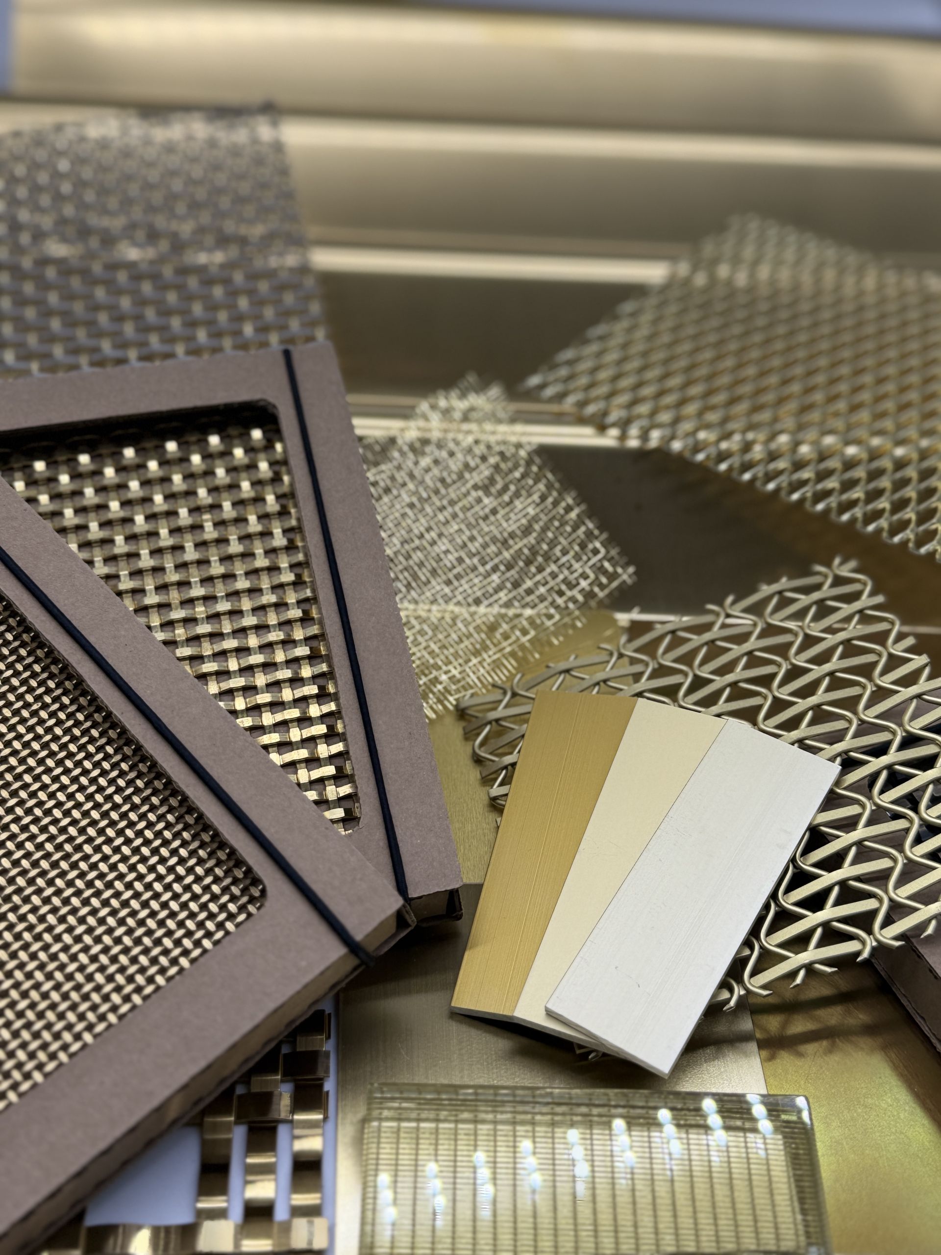 A selection of brass profiled metal, woven meshes in cardboard boxes, brass metal swatches and delicate woven mesh in brass